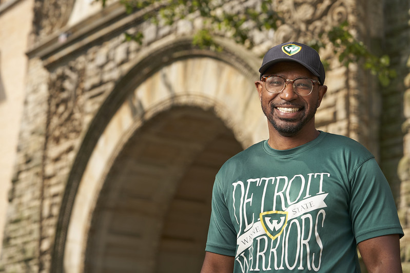 Wayne State University student wearing a green Detroit Warriors in front of the Old Main entrance