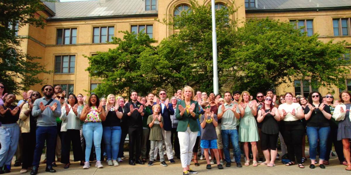 group of people standing in front of Old Main making a W with their hands